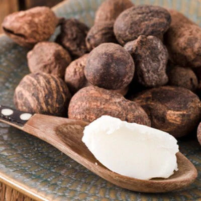 nuts of karité trees sitting on a table next to a wooden spoon with scoop of shea butter